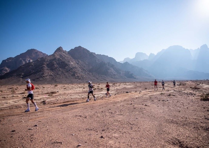 Trail Ultramarathon Runners running through the desert with rocky mountains surrounding them