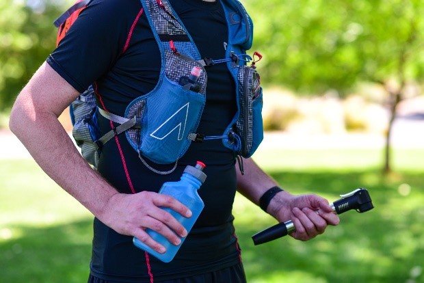 a runner wearing a hydration pack and holding a bottle in one hand and a screw in the other