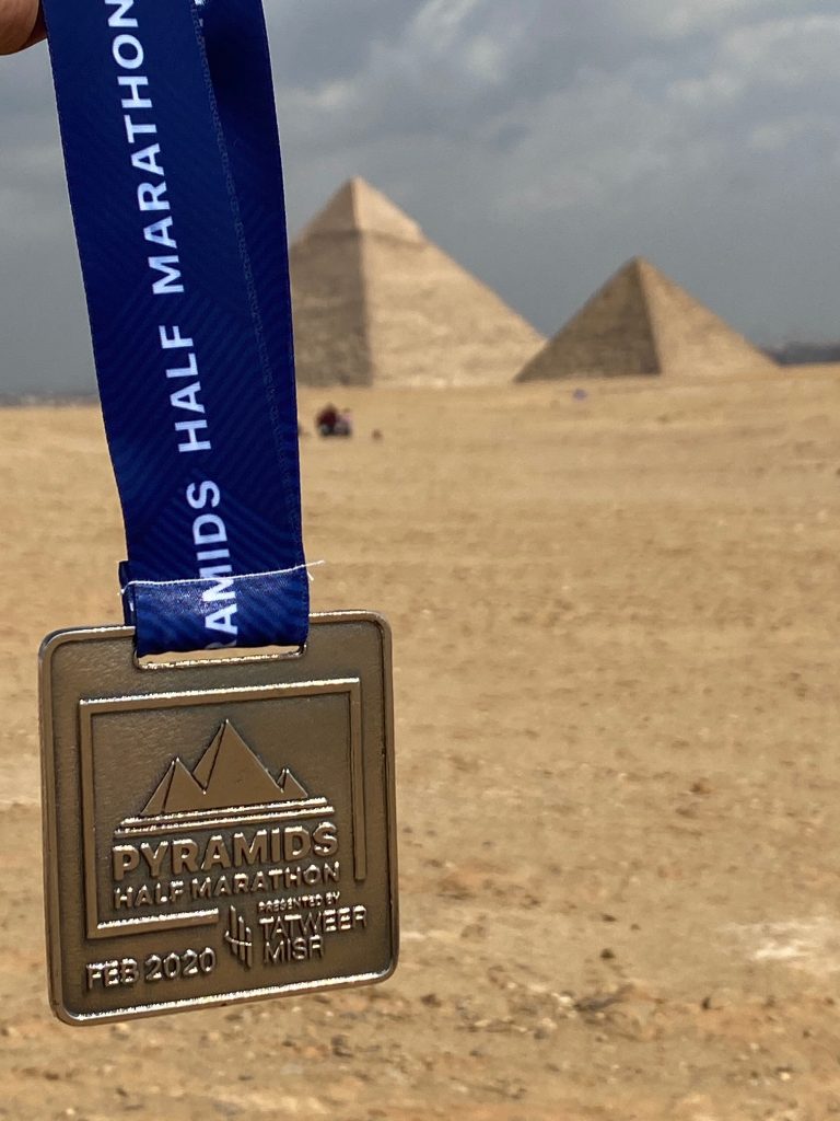 pyramids half marathon medal and the pyramids of giza in the background
